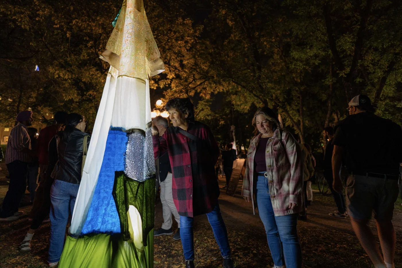 people standing looking at glowing garments made of pieces of fabric and cloth hanging from trees