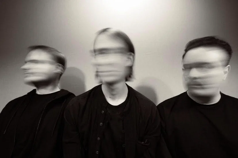three people standing with faces blurred in greyscale